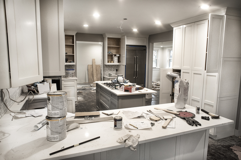 Messy home kitchen during remodeling with cabinet doors open cluttered with paint cans and tools, granite counter tops, appliances